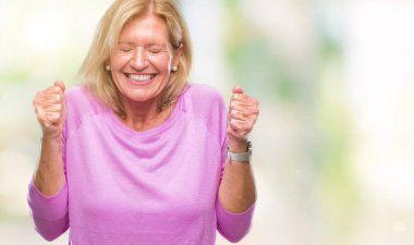 Orta yaş sarışın kadın izole arka kolları olan başarı için heyecan üzerinde zafer kutluyor gülümseyen kaldırdı. Kazanan kavramı.