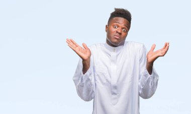Geleneksel djellaba üzerinde giyen genç Arapça Afrika adam arka plan clueless ve şaşkın bir ifadeyle kollar ve eller kaldırdı izole. Şüphe kavramı.