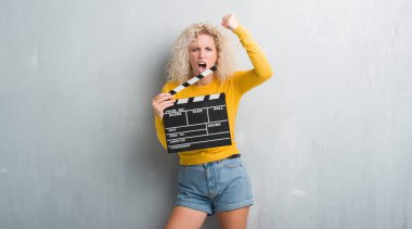 Sarışın genç kadın grunge üzerinde gri duvar calpboard film rahatsız ve öfke, çılgın ve yükseltilmiş el, öfke kavramı ile diye bağıran ile sinirli bağırarak holding