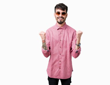 Yakışıklı delikanlı izole arka plan kutlama üzerinde güneş gözlüğü takıyor şaşırttı ve başarı için kaldırdı kollarını açarak hayret ve gözleri açık. Kazanan kavramı.