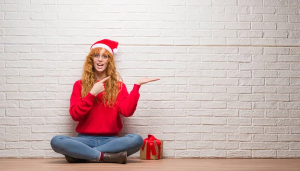 Young Redhead Woman Sitting Brick Wall Wearing Christmas Hat Amazed — Stock Photo, Image