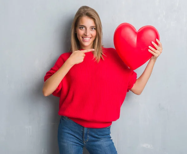 Hermosa Mujer Joven Sobre Pared Gris Grunge Sosteniendo Corazón Rojo — Foto de Stock