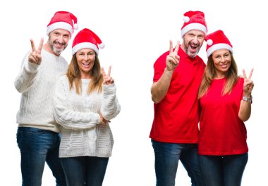 Kolaj bir orta yaş olgun güzel çift mutlu yüz zafer işareti yaparken kameraya göz kırpıyor ile gülümseyen beyaz izole arka plan üzerinde Noel şapka giyiyor. İki numaralı.