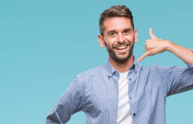 Genç yakışıklı yapıyor gülümseyen izole arka plan üzerinde beyaz t-shirt giyen adam telefon hareketi ile el ve parmak telefonda konuşuyor gibi. Kavramları iletişim.