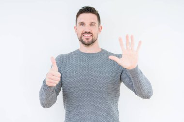 Gösterilen ve parmakları ile işaret izole arka plan üzerinde rahat kazak giyen genç yakışıklı adam kendinden emin ve mutlu gülümseyerek süre 6 numara.