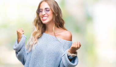 Gülümseyen ve başarı için çığlık izole arka plan çok mutlu ve heyecanlı kaldırdı, silah ile kazanan jest yapıyor üzerinde güneş gözlüğü takıyor güzel sarışın genç kadın. Kutlama kavramı.