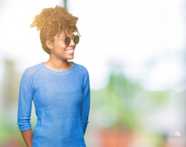 Güzel genç Afro-Amerikan kadın uzak tarafına yüzünde, doğal ifade gülümseme ile seyir izole arka plan üzerinde güneş gözlüğü takıyor. Kendine güvenen gülüyor.