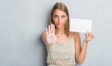 Grunge güzel genç kadın gri açık eliyle dur işareti ile ciddi ve kendine güvenen ifade, savunma jest yapıyor boş kartı tutan duvar