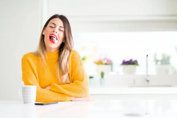 年轻美丽的女人在家里喝了一杯咖啡 用搞笑的表情伸出舌头高兴 情感概念 — 图库照片