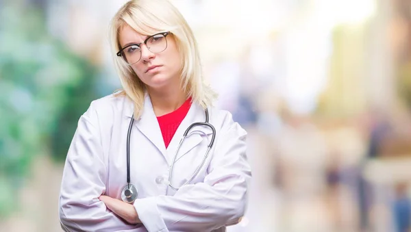 Young beautiful blonde doctor woman wearing medical uniform over isolated background skeptic and nervous, disapproving expression on face with crossed arms. Negative person.