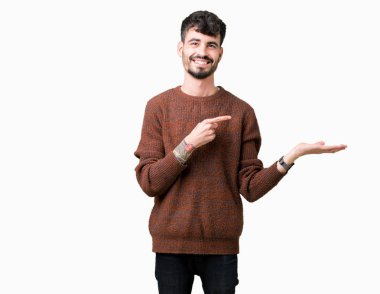 Hayret ve el ile sunulması ve parmak ile işaret ederken kameraya gülümseyen izole arka plan üzerinde kış kazak giyen genç yakışıklı adam.