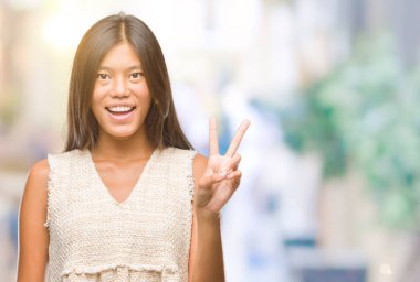 Genç Asyalı kadın mutlu yüz zafer işareti yaparken kameraya göz kırpıyor ile gülümseyen izole arka plan üzerinde. İki numaralı.