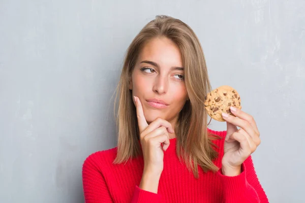 チョコレート チップ クッキー深刻な顔を考えて質問 非常に混乱して考えを食べるグランジ灰色の壁を越えて美しい若い女性 — ストック写真