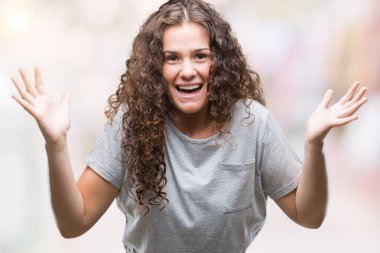 Güzel genç esmer kıvırcık saçlı kız rahat giyiyor izole arka plan kutluyor deli bakmak ve çığlık kaldırdı ve açık gözleri heyecanlı silah ile başarı için hayrete düşürdü. Kazanan kavramı