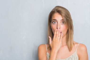Grunge gri duvar kapağı ağız elle hata, korku, ifade için utanç ile şok üzerinde duran güzel genç kadın sessizce, gizli kavramı korkuttu