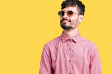 Genç yakışıklı adam uzak tarafına yüzünde, doğal ifade gülümseme ile seyir izole arka plan üzerinde güneş gözlüğü takıyor. Kendine güvenen gülüyor.