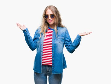 Güzel genç sarışın kadın üzerinde güneş gözlüğü takıyor arka plan clueless ve şaşkın bir ifadeyle kollar ve eller kaldırdı izole. Şüphe kavramı.