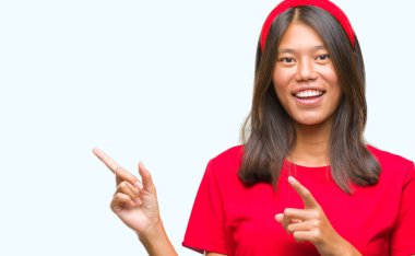 Asyalı genç bir kadın izole edilmiş arka planda gülümsüyor ve kameraya bakıyor iki eliyle ve parmaklarıyla kenarı işaret ediyor..