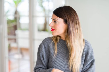 Genç güzel kadın giyiyor kış kazak evde doğal yüz emin gülümseme ile pozuyla profil rahatla tarafına, seyir.