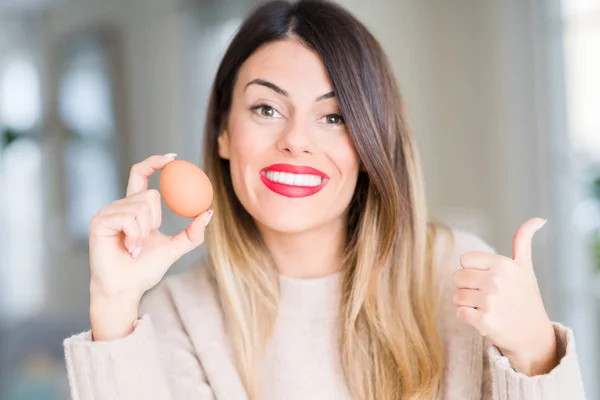 年轻美丽的女人拿着新鲜的鸡蛋在家里指着和显示与幸福的脸微笑的身边 — 图库照片