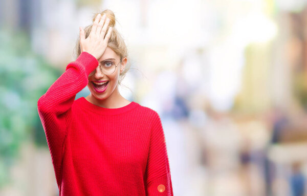 Young beautiful blonde woman wearing red sweater and glasses over isolated background surprised with hand on head for mistake, remember error. Forgot, bad memory concept.