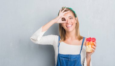 Mutlu yüz el parmaklarının arasından seyir göz üzerinde ok işaretiyle yapıyor gülümseyen ile meyve yeme grunge gri duvar güzel genç kadın