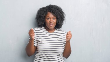 Genç Afro-Amerikan artı boyutu kadın üzerinde gri grunge duvar kutluyor şaşırttı ve başarı için kaldırdı kollarını açarak hayret ve gözleri açık. Kazanan kavramı.