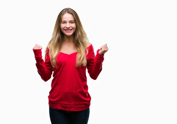 孤立した背景を祝う上赤いセーターを着ている若い美しいブロンドの女性驚いて腕を上げると成功のため驚くし 目を開きます 勝者の概念 — ストック写真