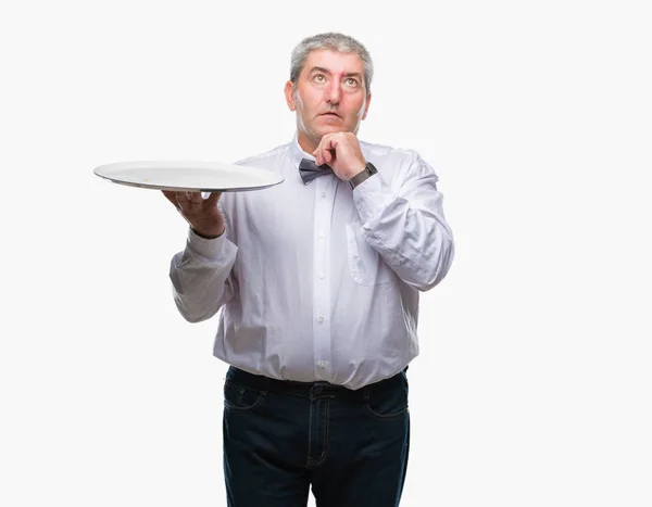 英俊的高级服务员拿着银盘在孤立的背景严重的脸思考问题 很困惑的想法 — 图库照片