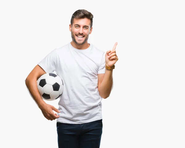 若いハンサムな男側の手と指で指す非常に幸せの孤立した背景にサッカー サッカー ボールを保持しています — ストック写真