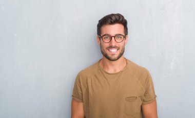 Yakışıklı genç adam gözlüklü mutlu ve güzel bir gülümseme ile yüzünde gri grunge duvarın üzerinden. Şanslı kişi.