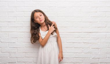 Genç İspanyol çocuk için beyaz tuğla duvar neşeli bir gülümseme ile el ve parmak kadar kameraya bakarak yüzündeki mutlu ve doğal ifade ile yan ile işaret eden yüz.