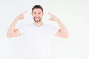 Casual beyaz t-shirt üzerinde izole giyen genç yakışıklı adam arka plan baş hem el parmak, harika bir fikir ya da düşünce, iyi bellek ile işaret eden gülen