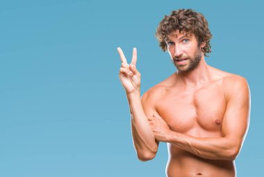 Yakışıklı İspanyol modeli adam seksi ve mutlu yüz zafer işareti yaparken kameraya göz kırpıyor ile gülümseyen izole arka plan üzerinde gömleksiz. İki numaralı.