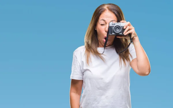 Middle age hispanic woman taking pictures using vintage photo camera over isolated background scared in shock with a surprise face, afraid and excited with fear expression