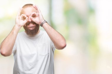 Dilini, parmaklarının arasından baktığını yapışmasını dürbün gibi ok jest yapıyor izole arka plan üzerinde rahat t-shirt giyen genç beyaz hipster adam. Deli ifade.