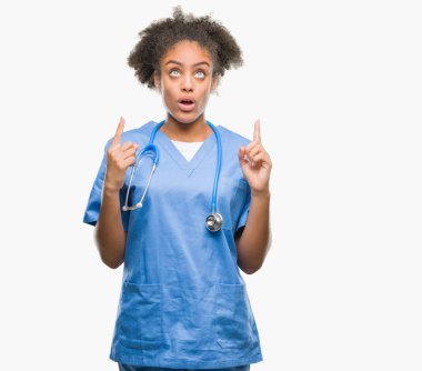 Genç afro Amerikalı doktor kadın izole arka plan üzerinden hayran ve yukarıya bakıp parmakları ile işaret şaşırttı ve silah kaldırdı.