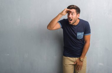 Gri grunge duvar çok mutlu ve gülümseyen uzakta el ile üzerine kafa seyir yakışıklı genç adam. Arama kavramı.