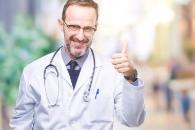 Orta yaş üst düzey ağarmış Doktor tıbbi üniforma izole geçmişi hareketi el ile mutlu yaşasın yapıyor giyen adam. Kameraya bakarak başarı gösteren ile ifade onaylama.