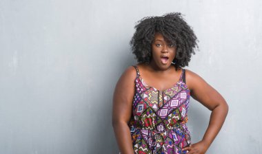 Gri grunge duvar korkuyor ve şok sürpriz ifade, korku ve heyecan yüz ile renkli elbise giyen genç Afro-Amerikan kadın.
