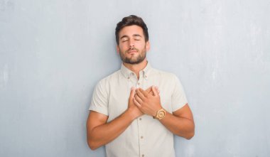 Göğüs kapalı gözler ve yüzünde minnettar jest ile yaz ile gömlek gülümseyen giyen gri grunge duvarın üzerinden yakışıklı genç eller. Sağlık kavramı.