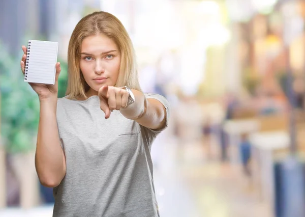 年轻的高加索妇女拿着空白笔记本在孤立的背景指向镜头和你 手的标志 积极和自信的手势从前面 — 图库照片
