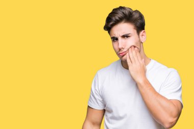 Diş ağrısı veya dişlerde dişlerle ilgili hastalık nedeniyle ağız acı ifadesi ile el ile dokunmak izole arka plan üzerinde beyaz t-shirt giyen genç yakışıklı adam. Diş hekimi kavramı.