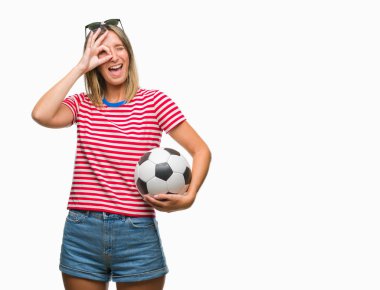 Mutlu yüz el parmaklarının arasından seyir göz üzerinde ok işaretiyle yapıyor gülümseyen izole arka plan üzerinde futbol futbol topu tutan genç güzel kadın