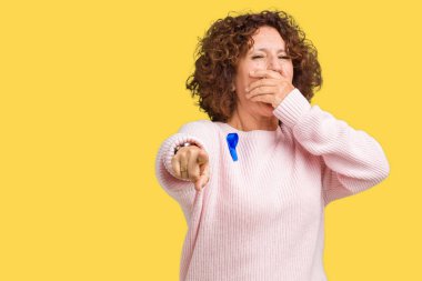Değiştirilebilir mavi renk şerit duyarlılığı izole üzerinde giyen orta ager üst düzey kadın gülme sizin arka plan, fotoğraf makinesi ile işaret eden parmak el ağzına, utanç ifadesi
