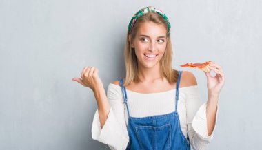 Güzel genç kadın işaret ve başparmak kadar mutlu yüz gülümseyen tarafı ile gösterilen pepperoni pizza dilimi yemek grunge gri duvarın üzerinden