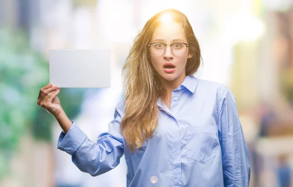 Young beautiful blonde business woman holding blank card over isolated background scared in shock with a surprise face, afraid and excited with fear expression