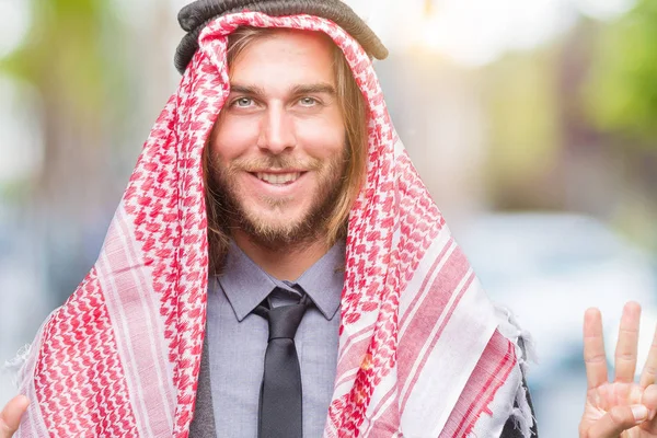 Young handsome arabian man with long hair wearing keffiyeh over isolated background showing and pointing up with fingers number eight while smiling confident and happy.