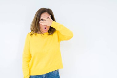 Yüz ve gözler el ile kapsayan şok bakmak izole arka plan üzerinde sarı kazak giyen güzel orta yaş kadın mahcup ifadeyle parmaklarımın arasından seyir.