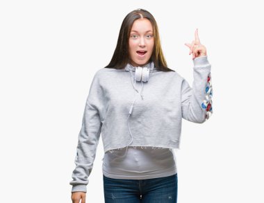 Başarılı fikirle izole arka plan işaret parmağı üzerinde kulaklık giyen genç güzel beyaz öğrenci kadın. Çıktıktan ve mutlu. Bir numara.